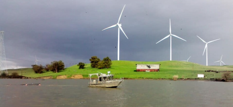 boat on river, cloudy sky, wind generators on background hills