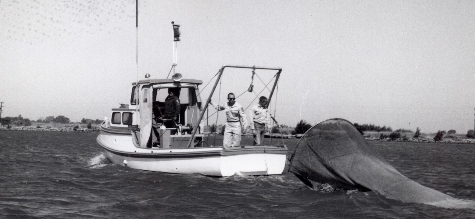 monochrome photo of two men on a boat with net trailing behind